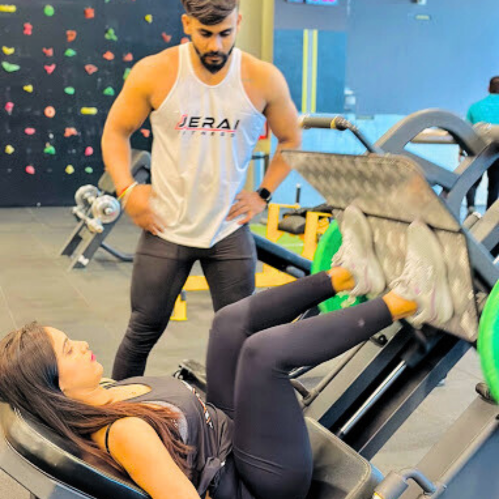 "Personal trainer supervising a woman performing leg press exercises on a weight machine in a modern gym during a strength training workout."