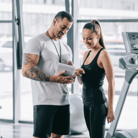 "Personal fitness trainer discussing a customized workout plan with a gym member using a tablet in a modern fitness center."