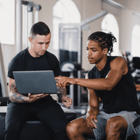 "Personal trainer reviewing a fitness plan on a laptop with a gym member during a one-on-one coaching session in a modern fitness center."