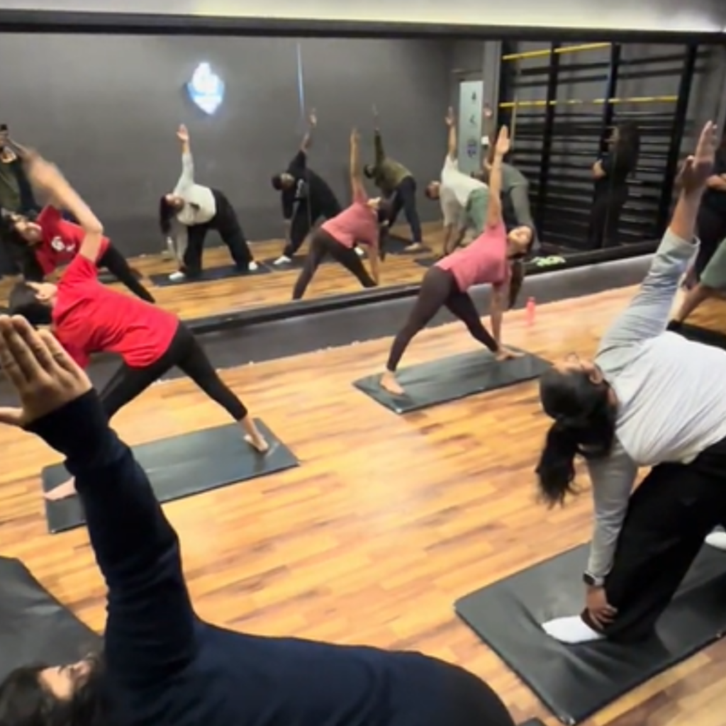 "Group fitness class participants performing triangle pose (Trikonasana) on yoga mats in a modern studio with mirrored walls during a guided yoga session.